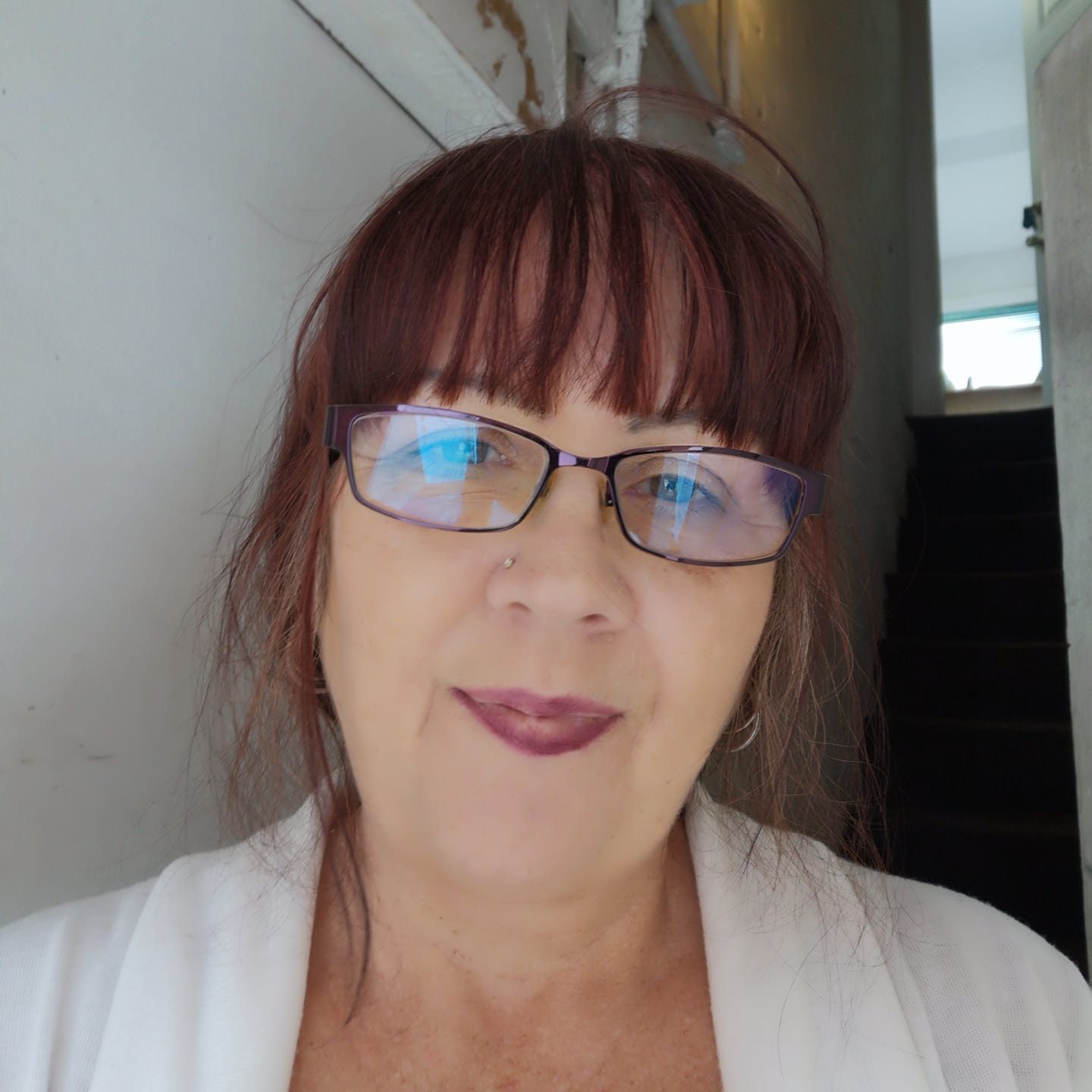 Woman with glasses and a white top standing indoors, smiling.